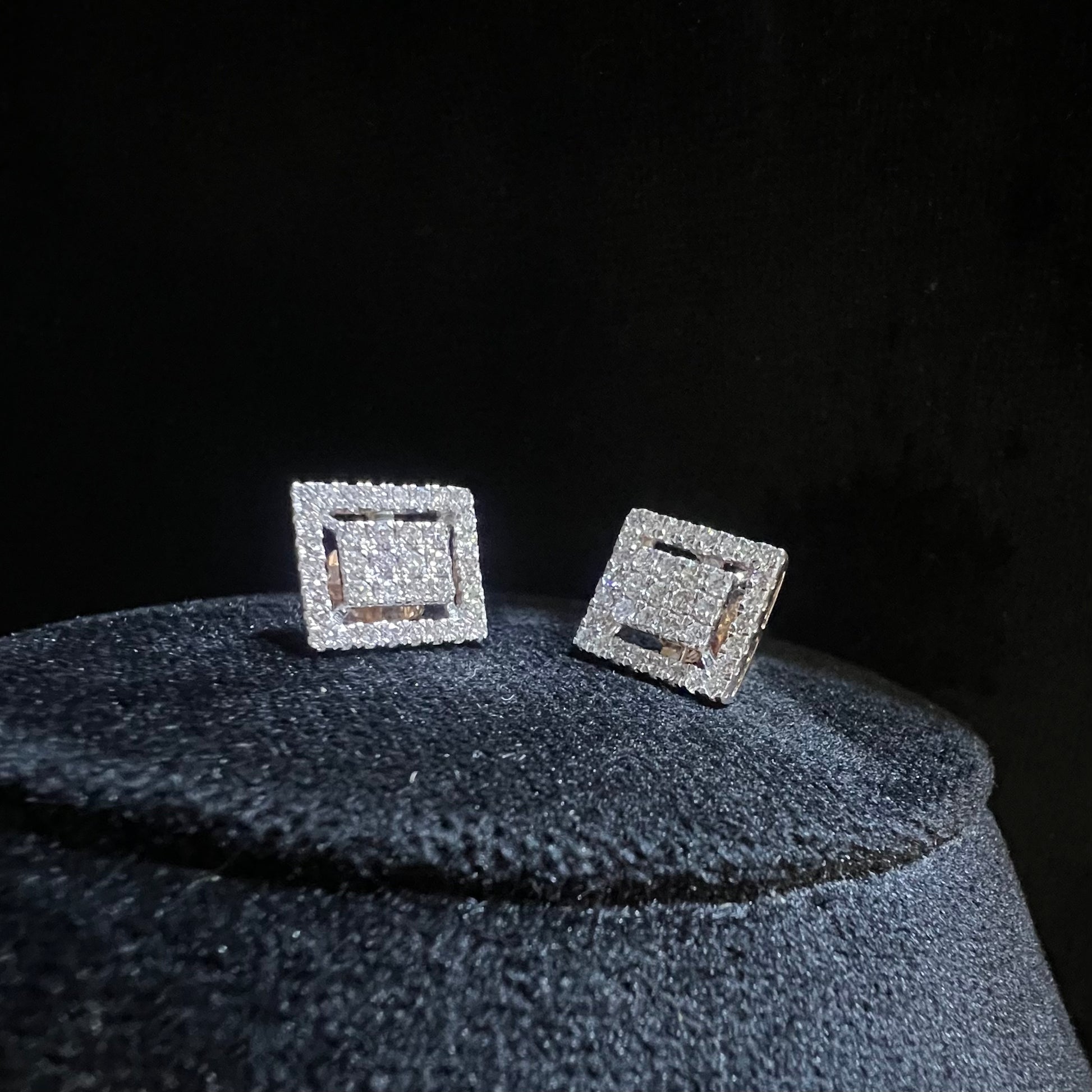 A pair of diamond stud earrings set in a gold casing, displayed against a reflective surface.
