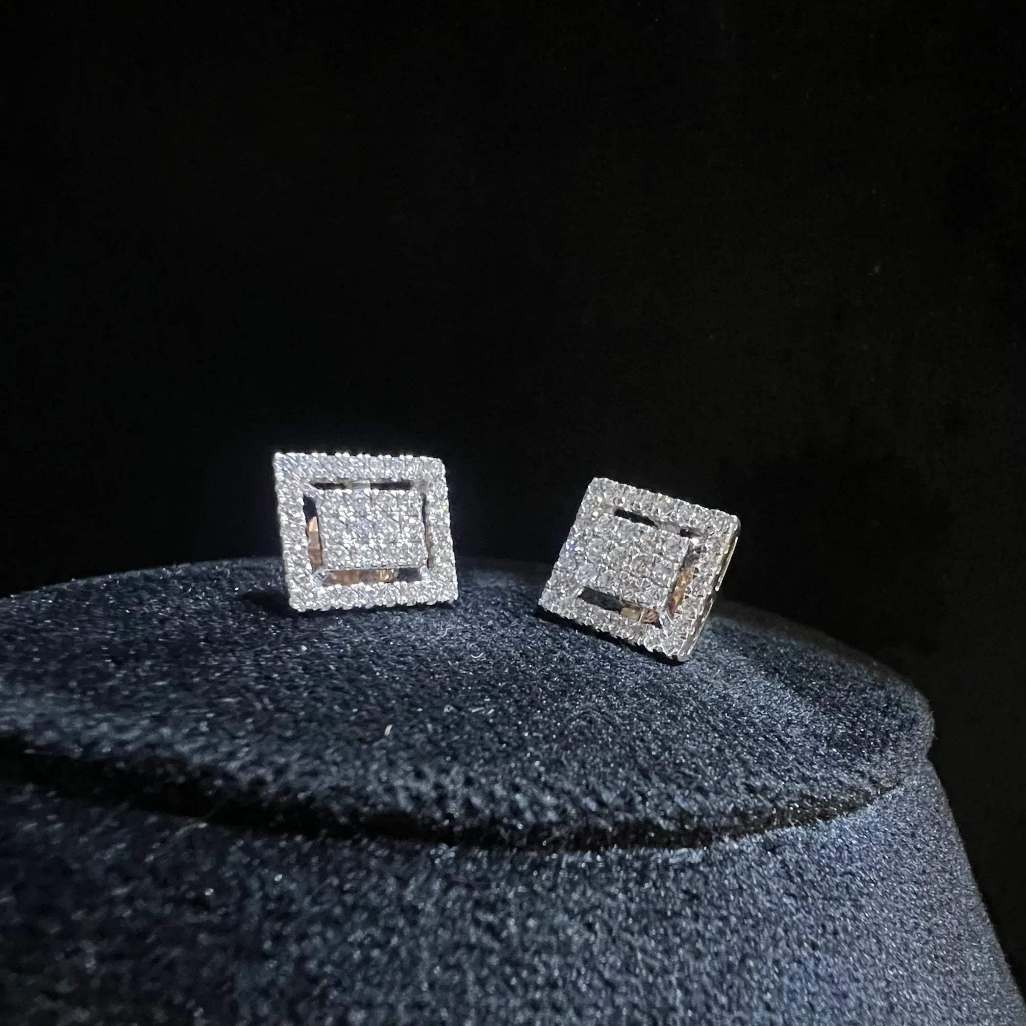 A pair of diamond stud earrings set in a gold casing, displayed against a reflective surface.