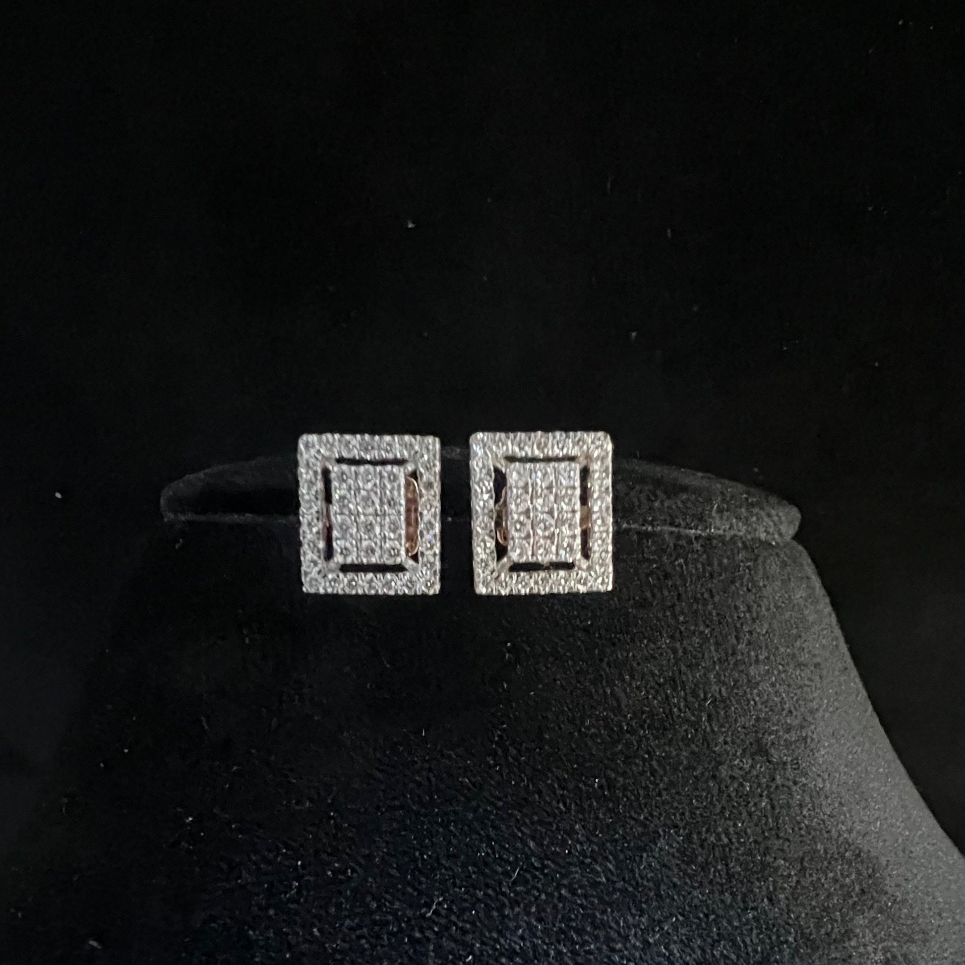 A pair of diamond stud earrings set in a gold casing, displayed against a mannequin stand.