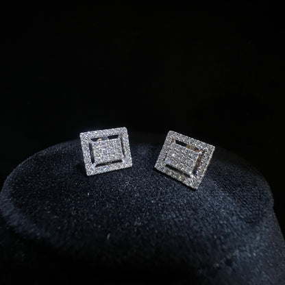 A pair of diamond stud earrings set in a gold casing, displayed against a mannequin stand.
