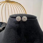 A pair of gold diamond earrings with a round cut design, placed on a mannequin stand with a decorative background.