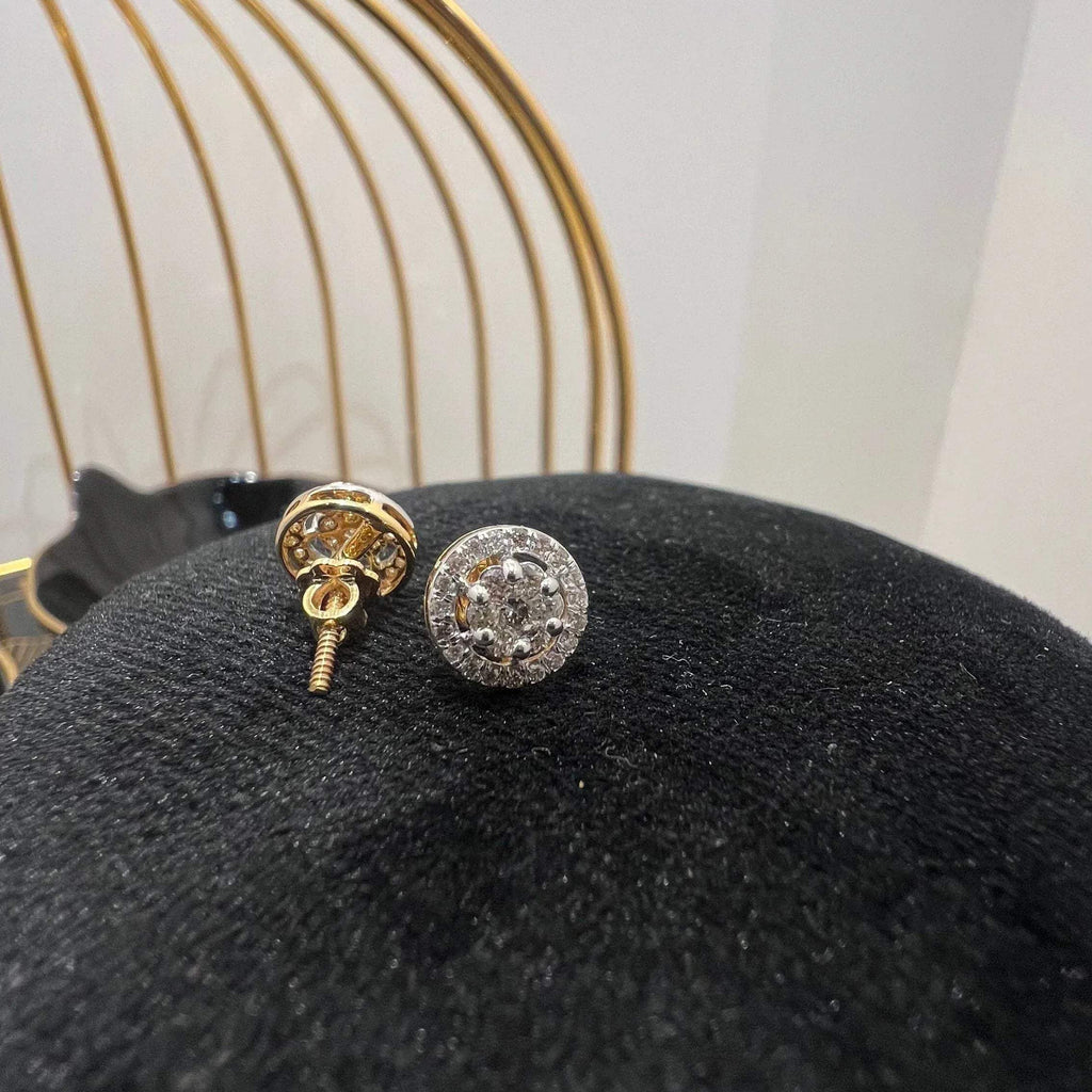 A pair of gold diamond earrings with a round cut design, placed on a mannequin stand with a decorative background.