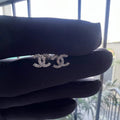 A pair of gold diamond earrings held on a mannequin hand, with a clear and bright design.