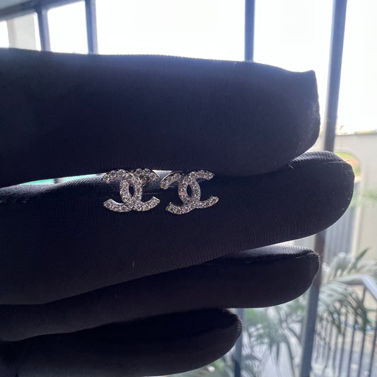 A pair of gold diamond earrings held on a mannequin hand, with a clear and bright design.