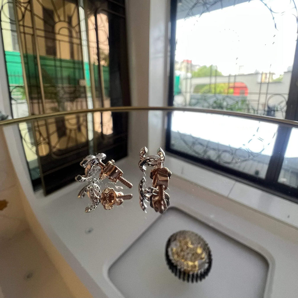 A pair of gold diamond earrings held on a reflective surface, with a clear and bright design.