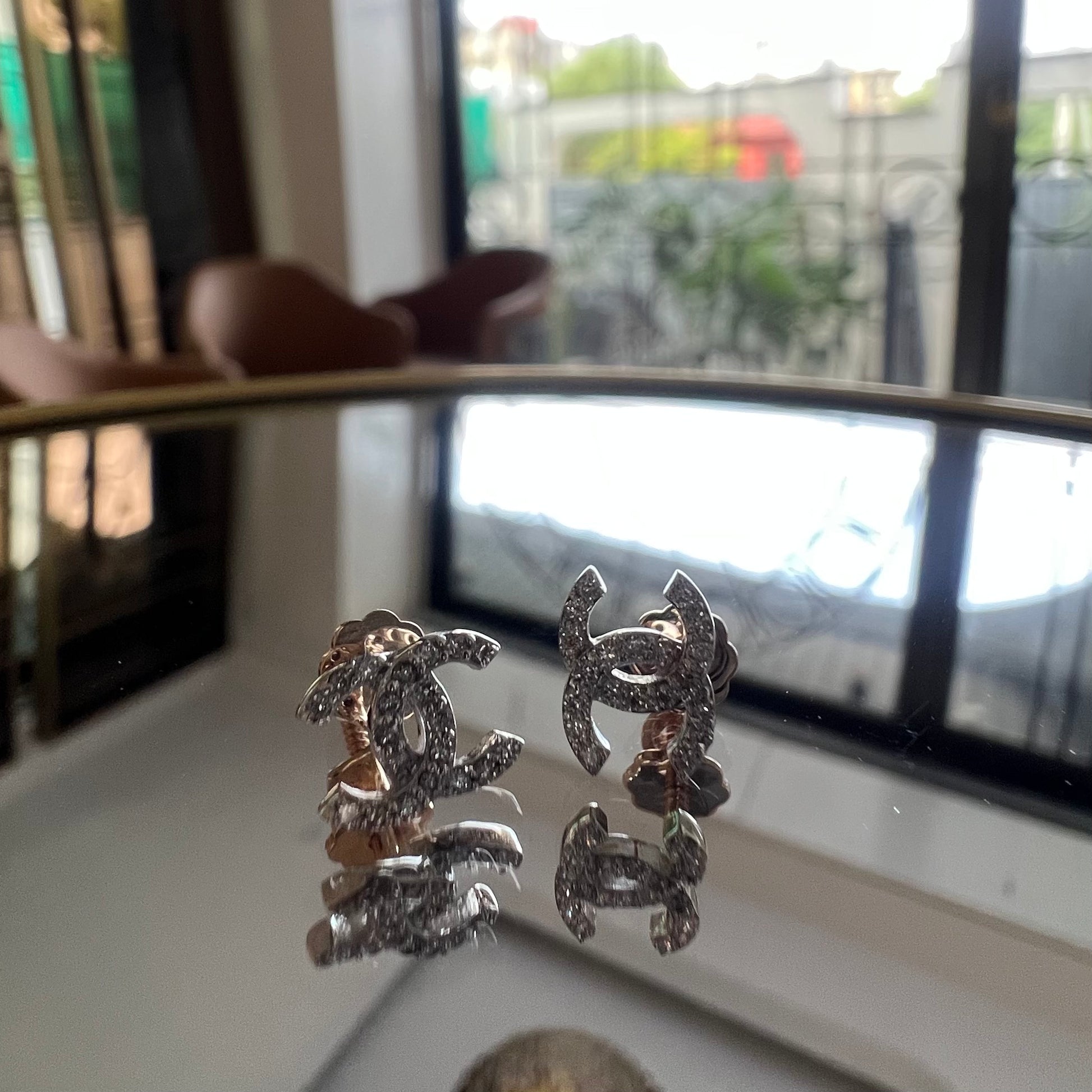 A pair of gold diamond earrings held on a reflective surface, with a clear and bright design.