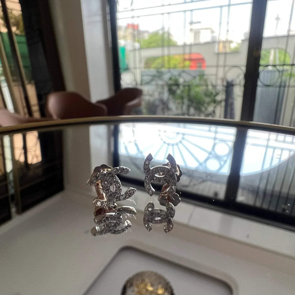 A pair of gold diamond earrings held on a reflective surface, with a clear and bright design.