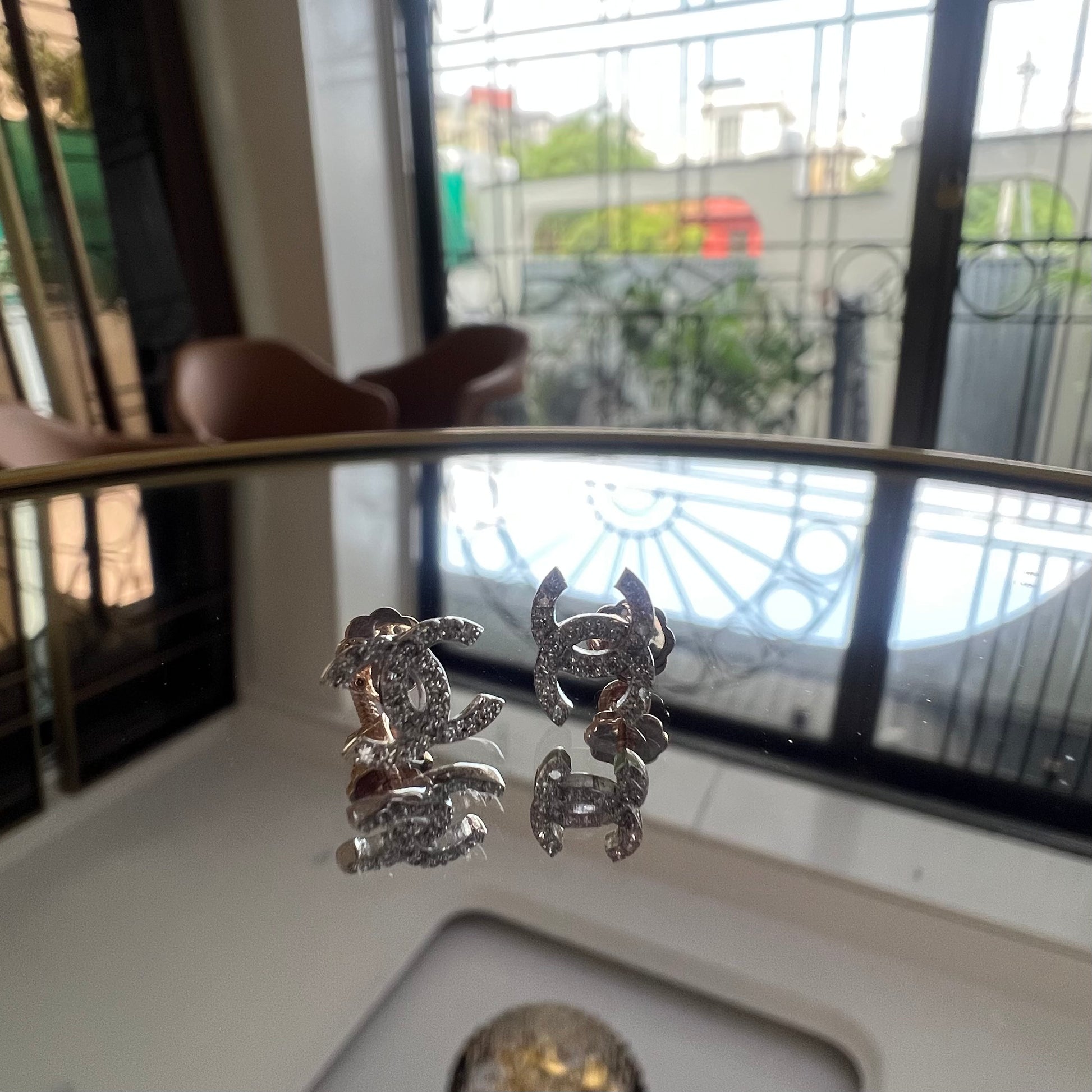 A pair of gold diamond earrings held on a reflective surface, with a clear and bright design.
