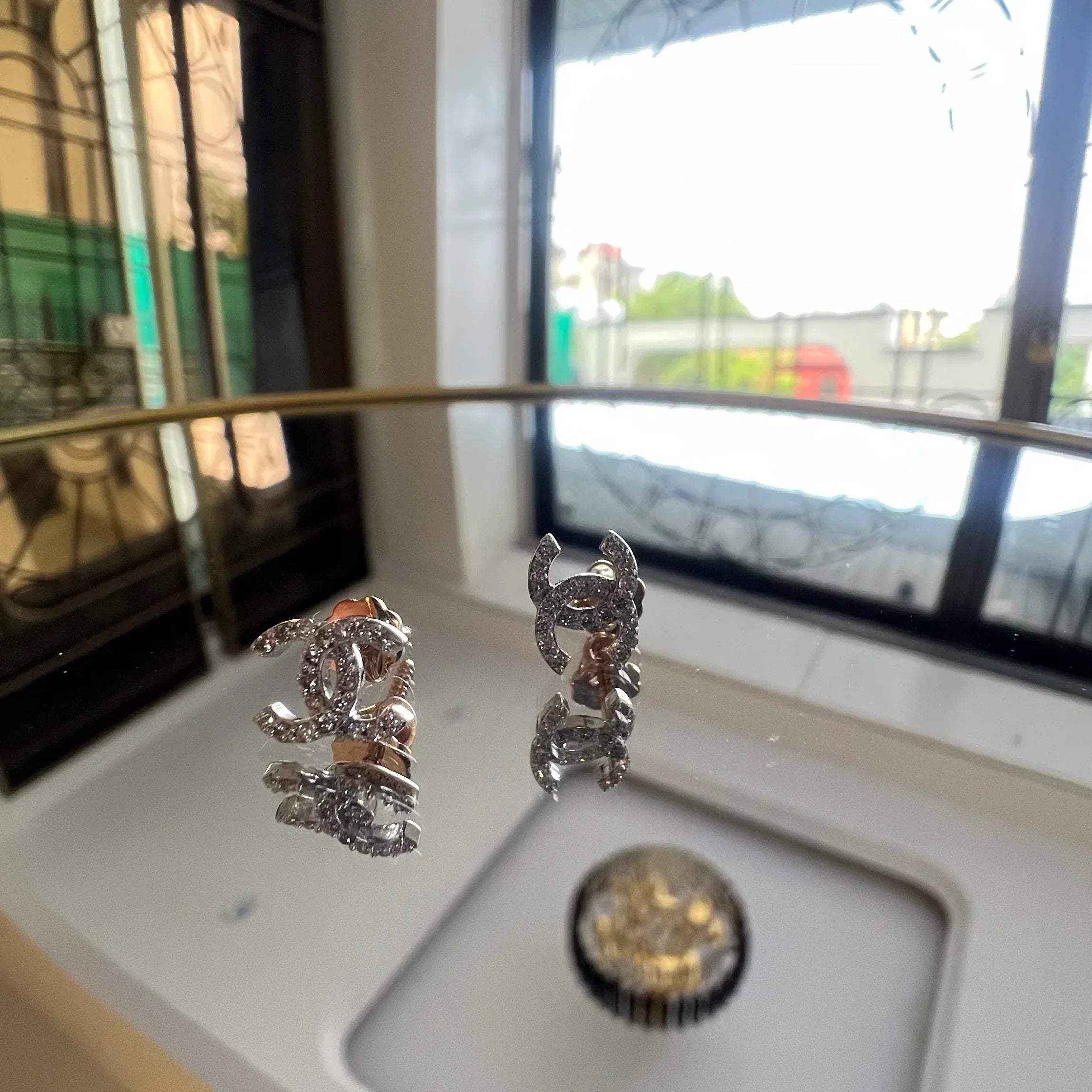 A pair of gold diamond earrings held on a reflective surface, with a clear and bright design.