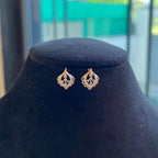 A pair of diamond stud earrings displayed on a black stand, with a mannequin jewelry stand in the background.