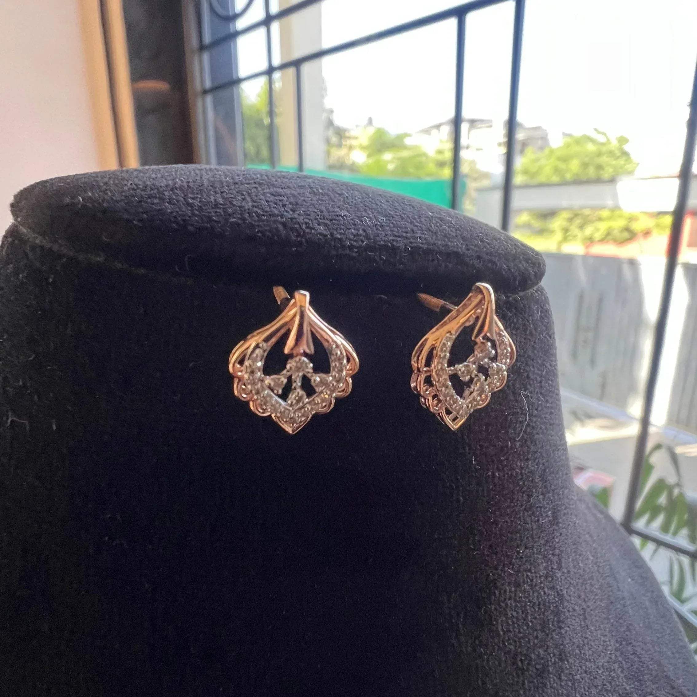 A pair of diamond stud earrings displayed on a black stand, with a mannequin jewelry stand in the background.