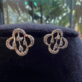 A pair of handcrafted 14k gold diamond stud earrings displayed on a black stand.