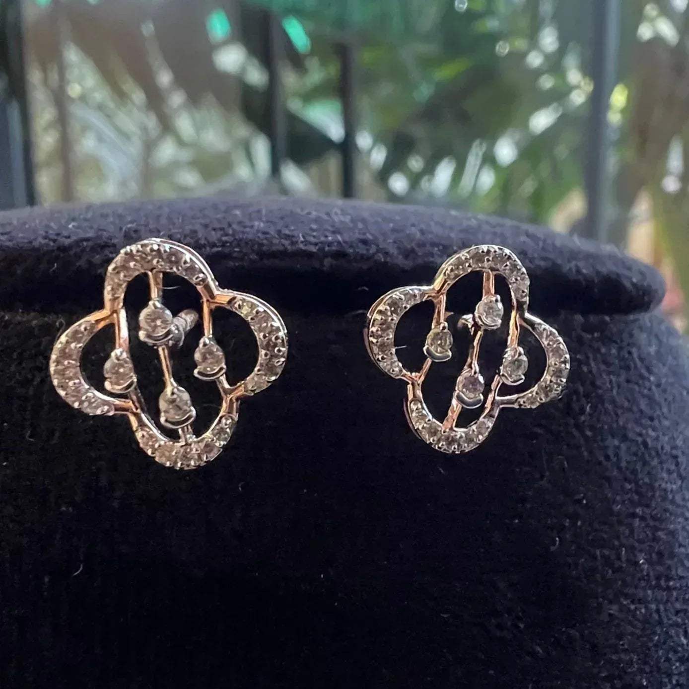 A pair of handcrafted 14k gold diamond stud earrings displayed on a black stand.