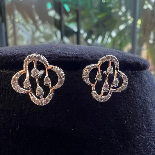 A pair of handcrafted 14k gold diamond stud earrings displayed on a black stand.