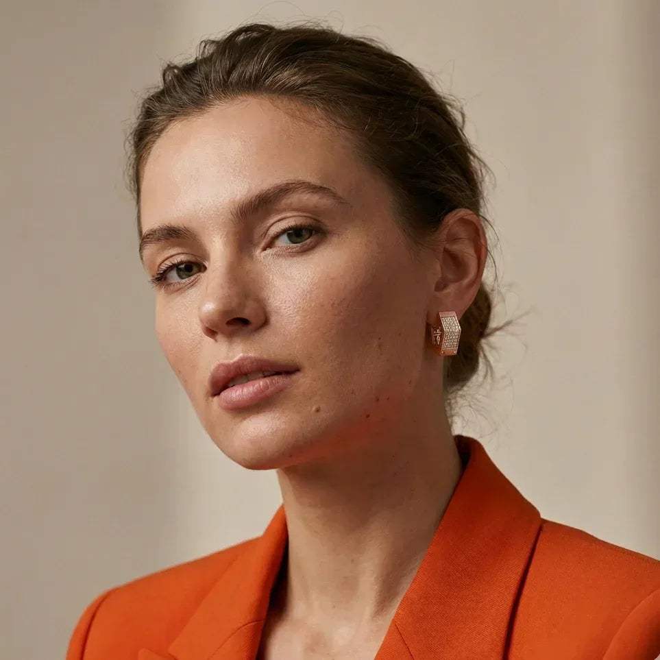 Woman wearing an orange blazer with real diamond earring with a neutral background