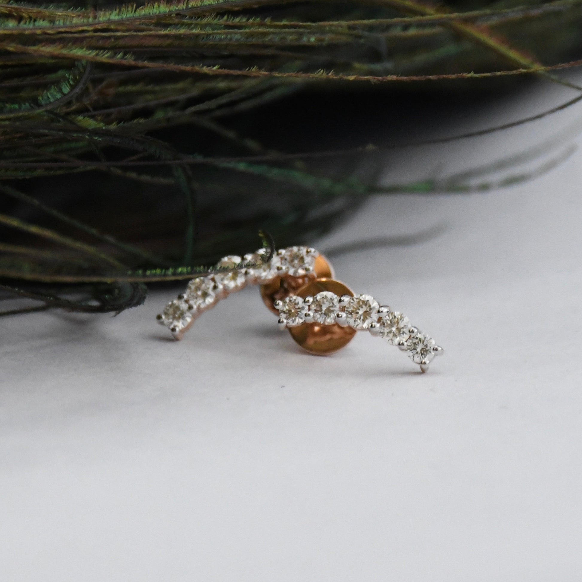 real diamond stud earrings on a white surface with greenery in the background