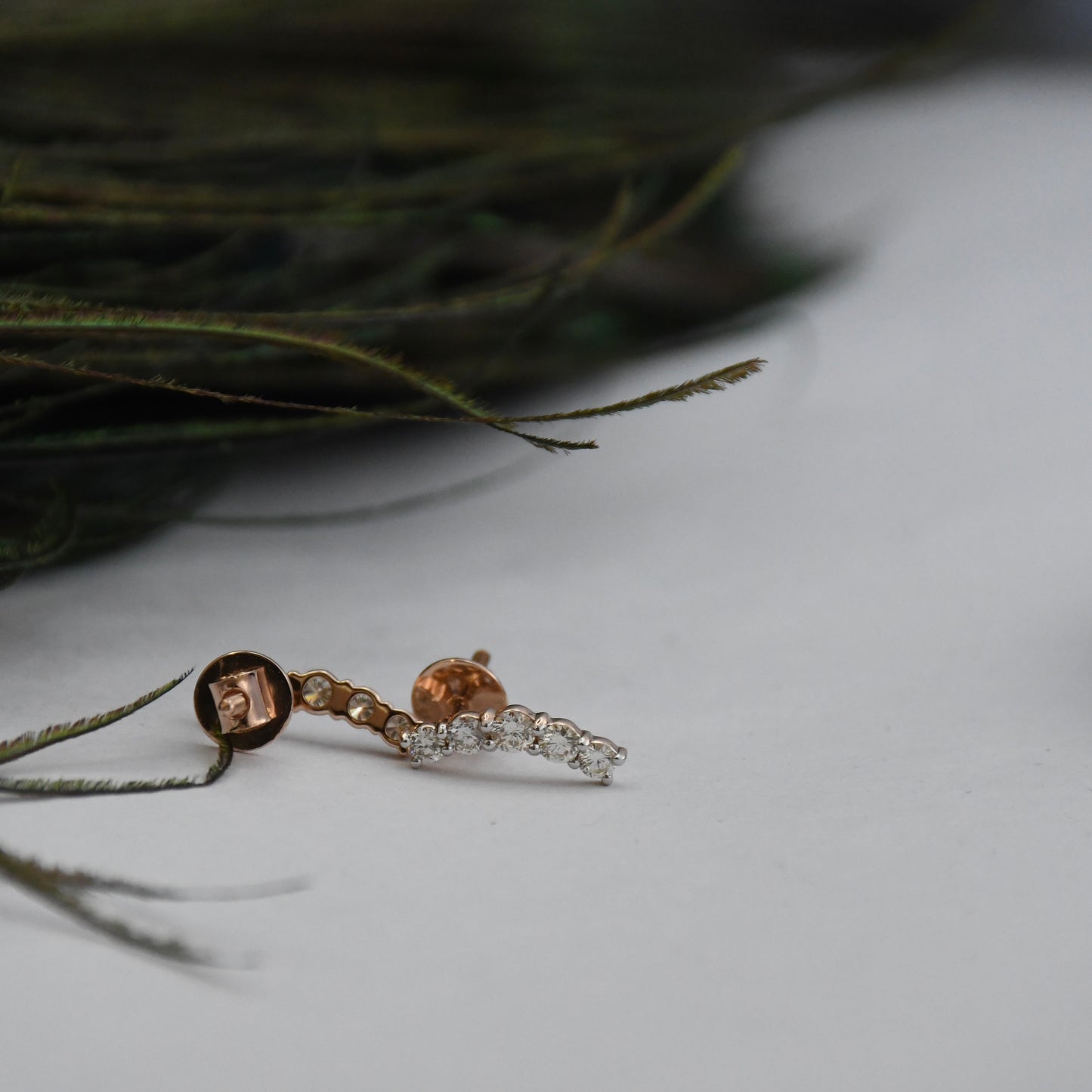real diamond studs in rose gold on a white surface with green leaves.