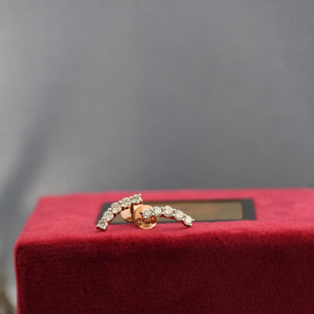 Gold earrings with real diamonds on a red cushion against a gray background
