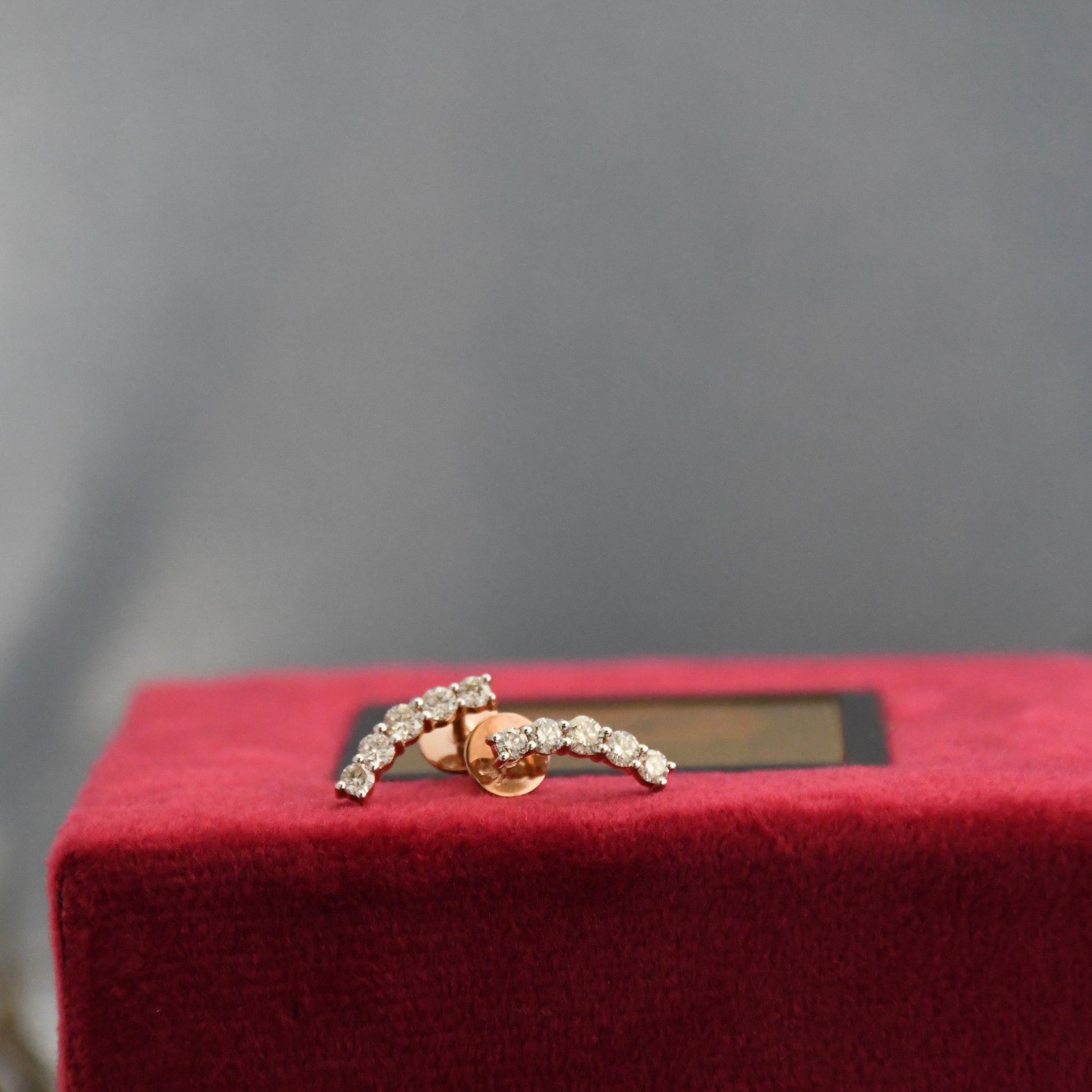Gold earrings with real diamonds on a red cushion against a gray background