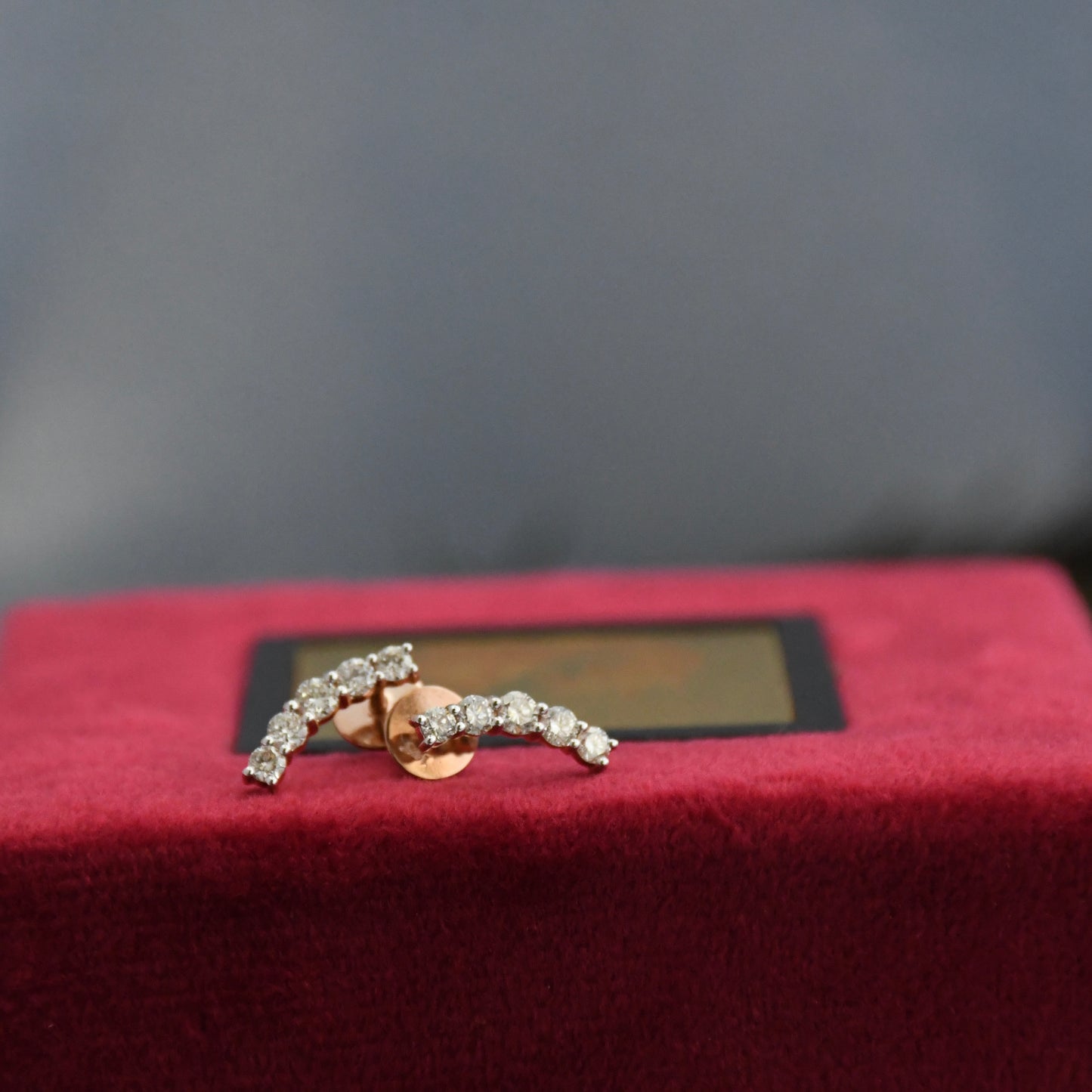 Gold earrings with real diamonds on a red cushion against a dark background