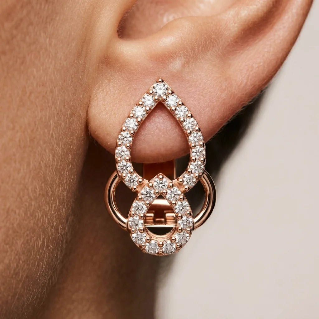 Rose gold earrings with clear diamonds worn on an ear against a neutral background