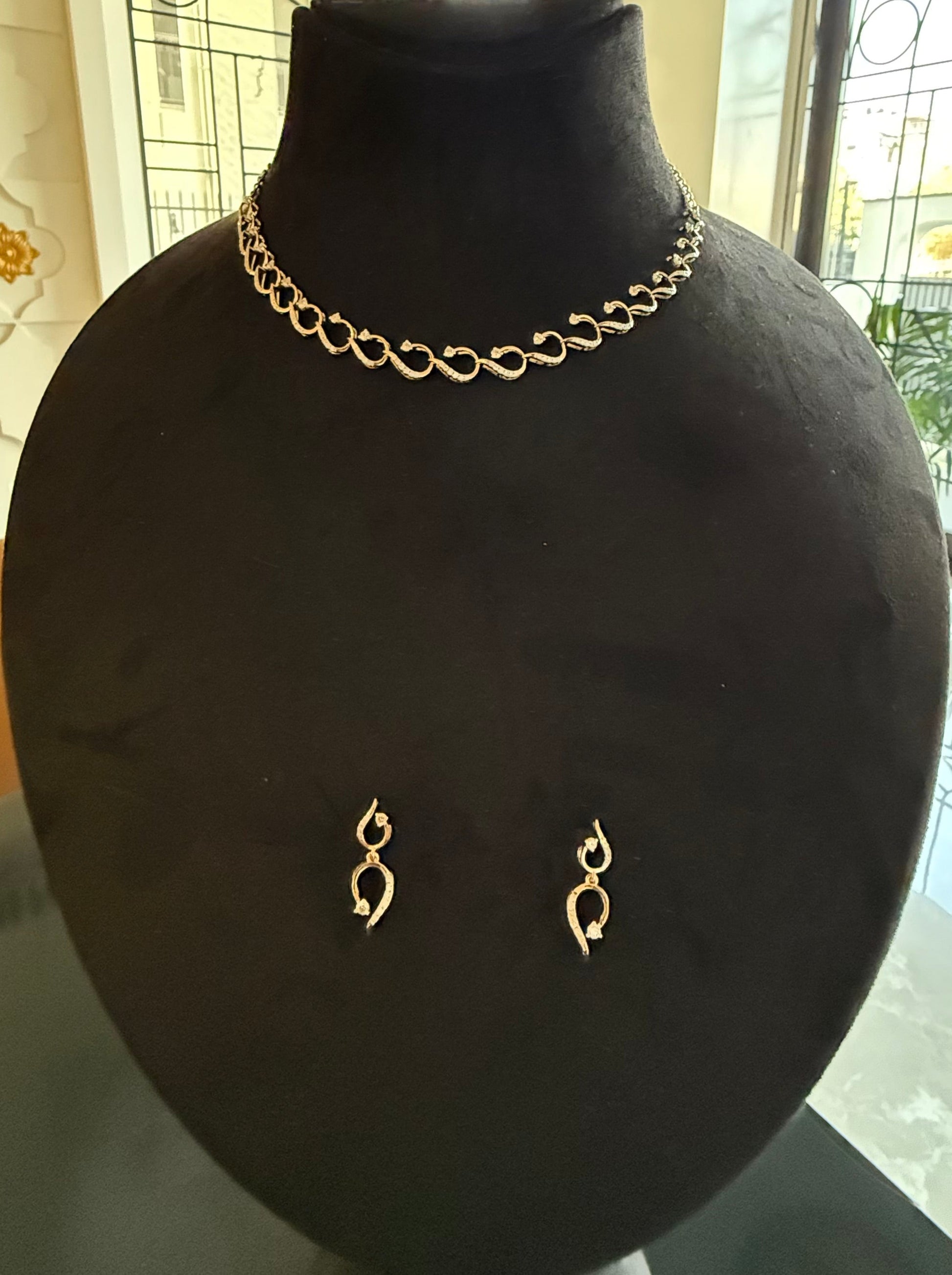A gold diamond necklace with a chain link design, displayed on a mannequin bust, accompanied by a pair of matching earrings with a geometric design.