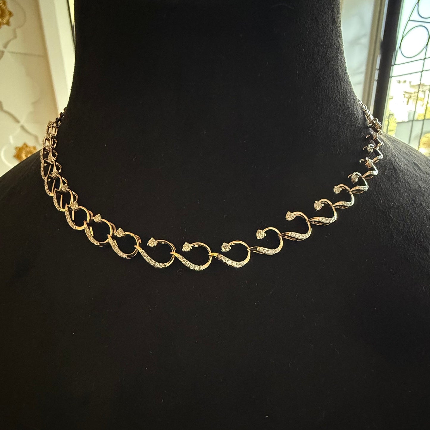 A gold diamond necklace with a chain link design, displayed on a mannequin bust.