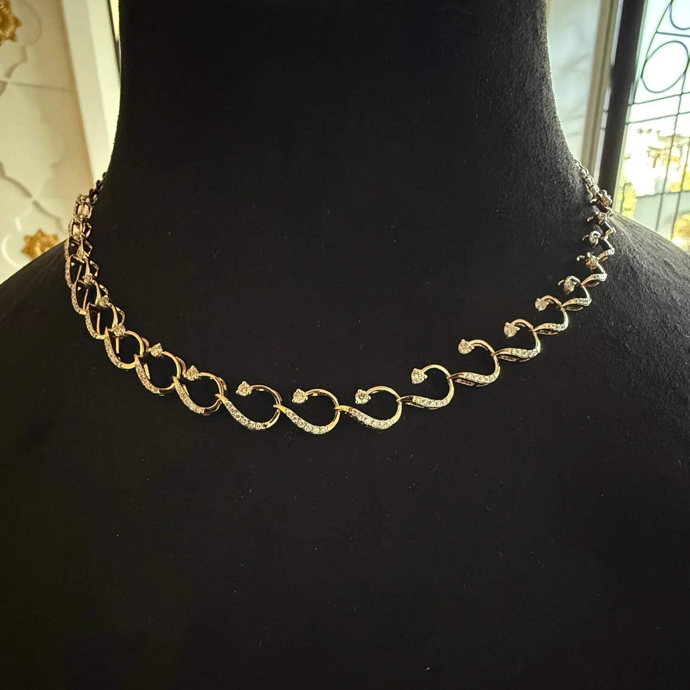 A gold diamond necklace with a chain link design, displayed on a mannequin bust.