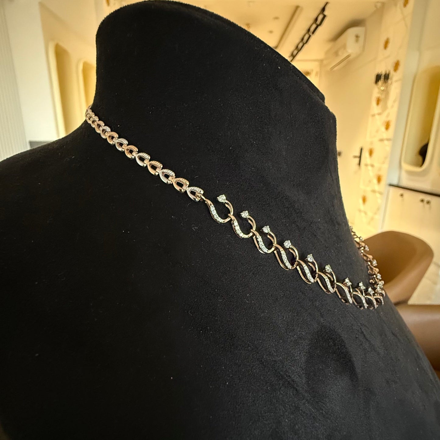 A gold diamond necklace with a chain link design, displayed on a mannequin bust.