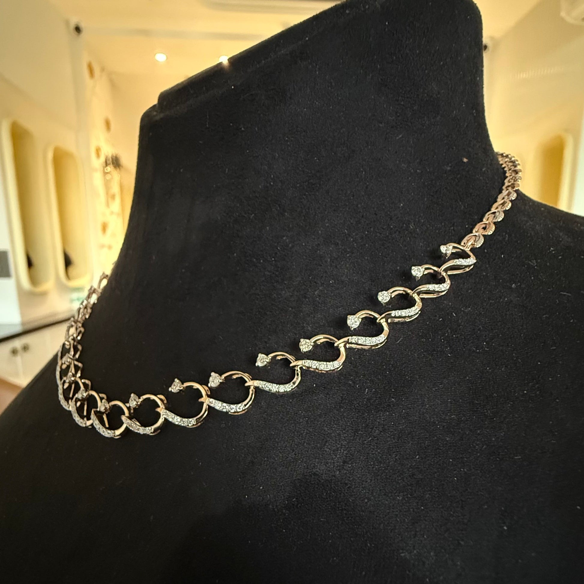 A gold diamond necklace with a chain link design, displayed on a mannequin bust.