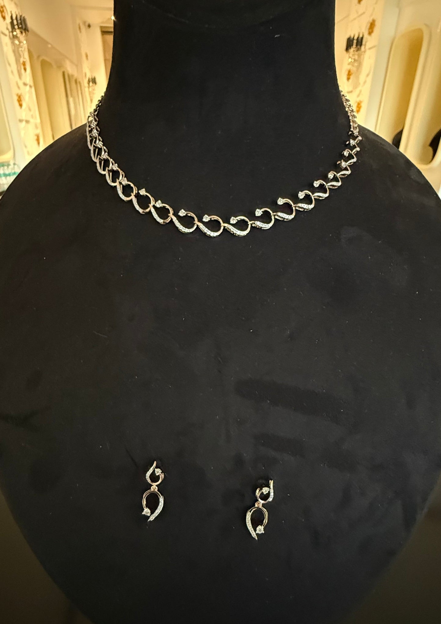 A gold diamond necklace with a chain link design, displayed on a mannequin bust, accompanied by a pair of matching earrings with a geometric design.