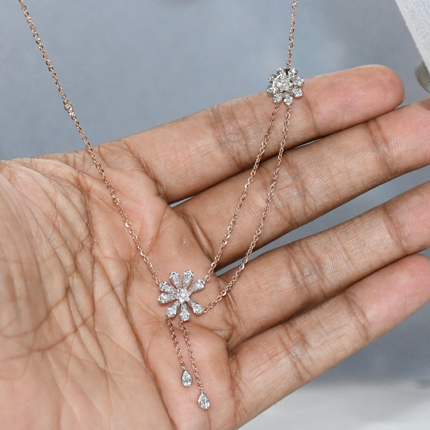 Rose gold necklace with floral pendant held in a hand against a neutral background