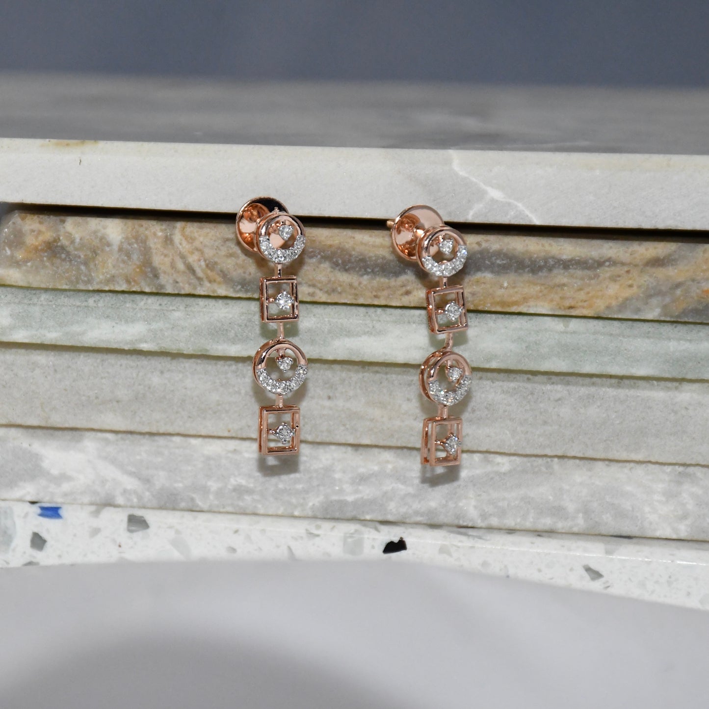 Rose gold earrings with diamonds on a marble surface