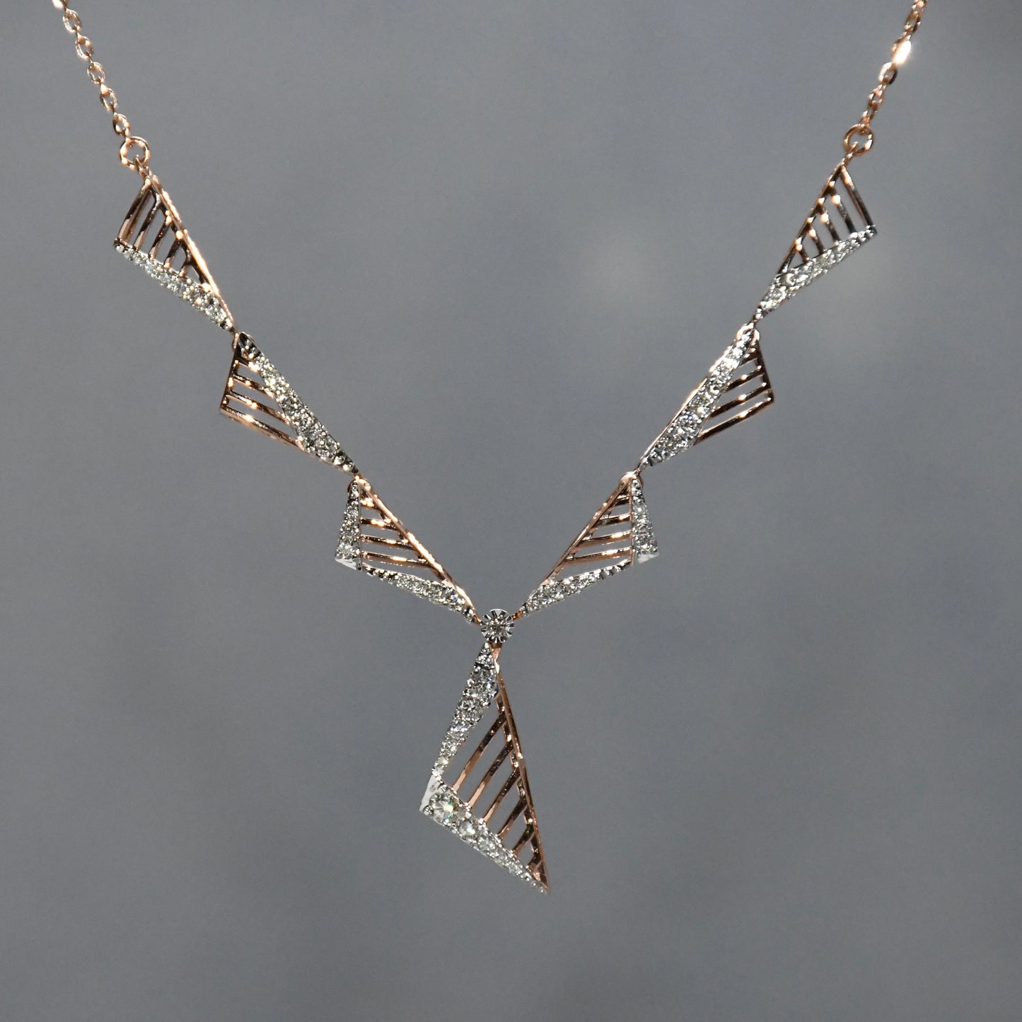 Geometric diamond necklace with triangular design on a gray background.