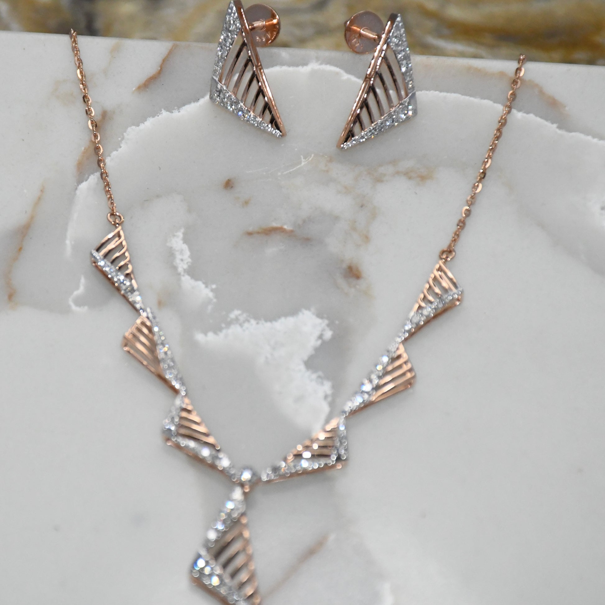 Gold diamond necklace and earrings on a marble surface.