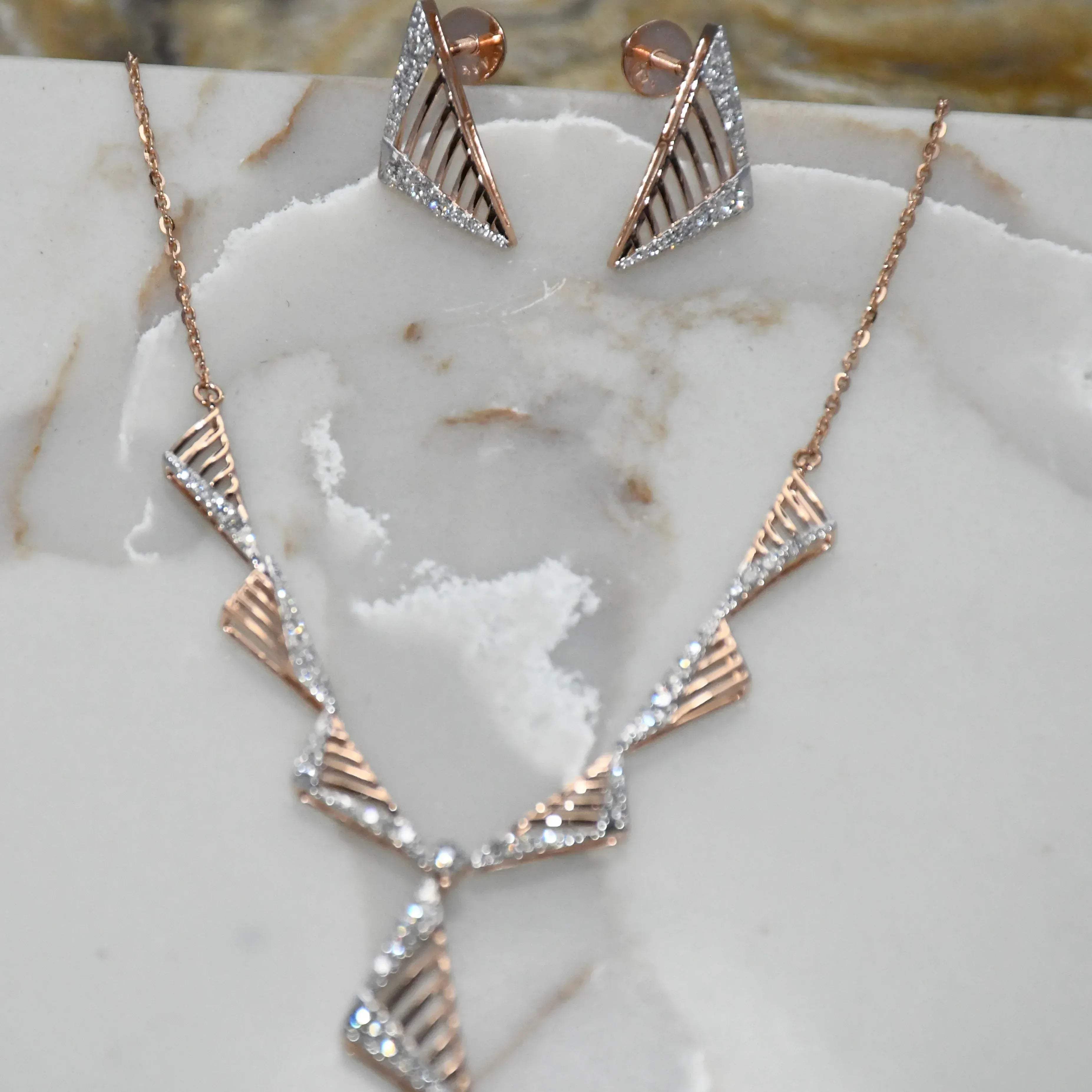 Gold diamond necklace and earrings on a marble surface.