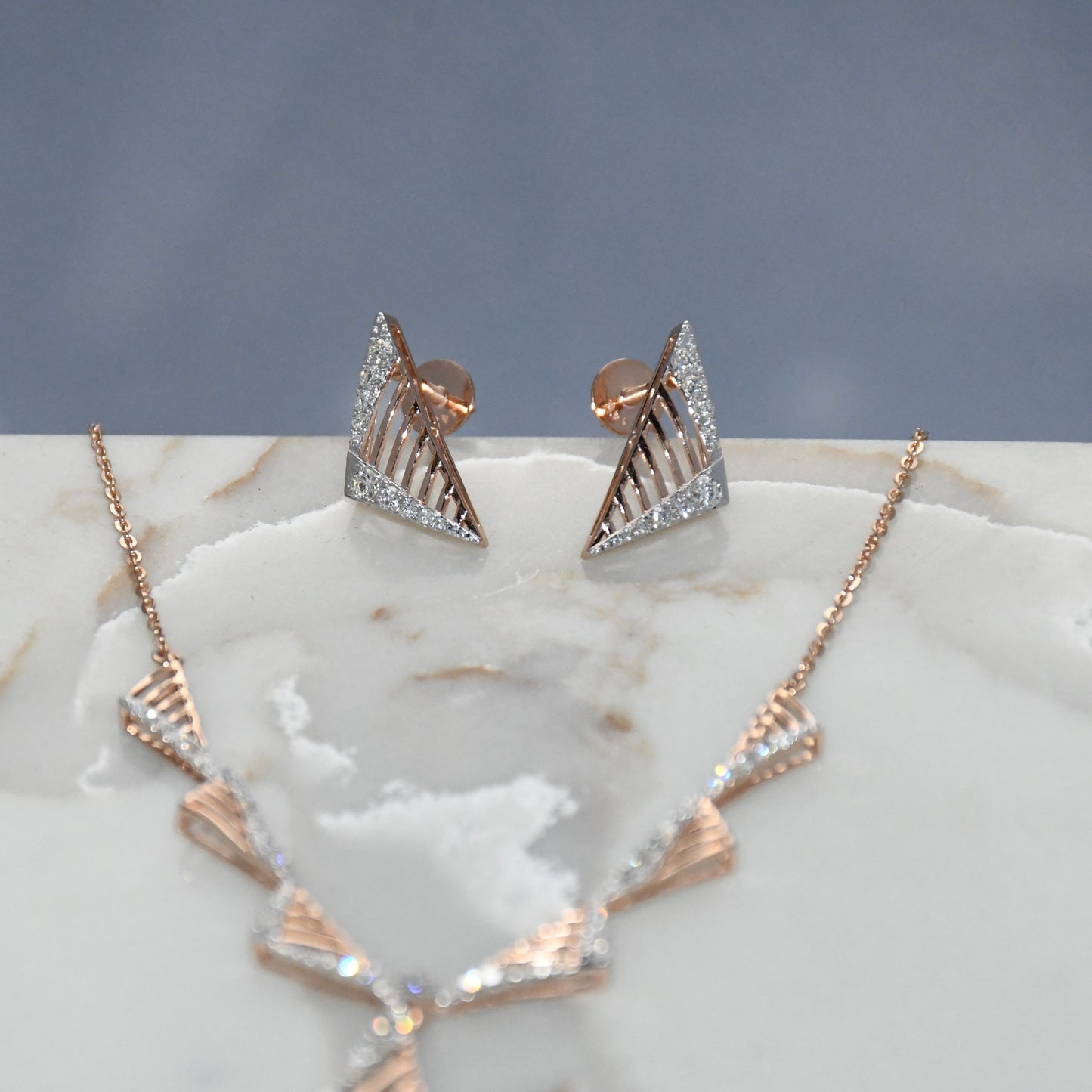 Gold diamond necklace and earrings on a marble surface.