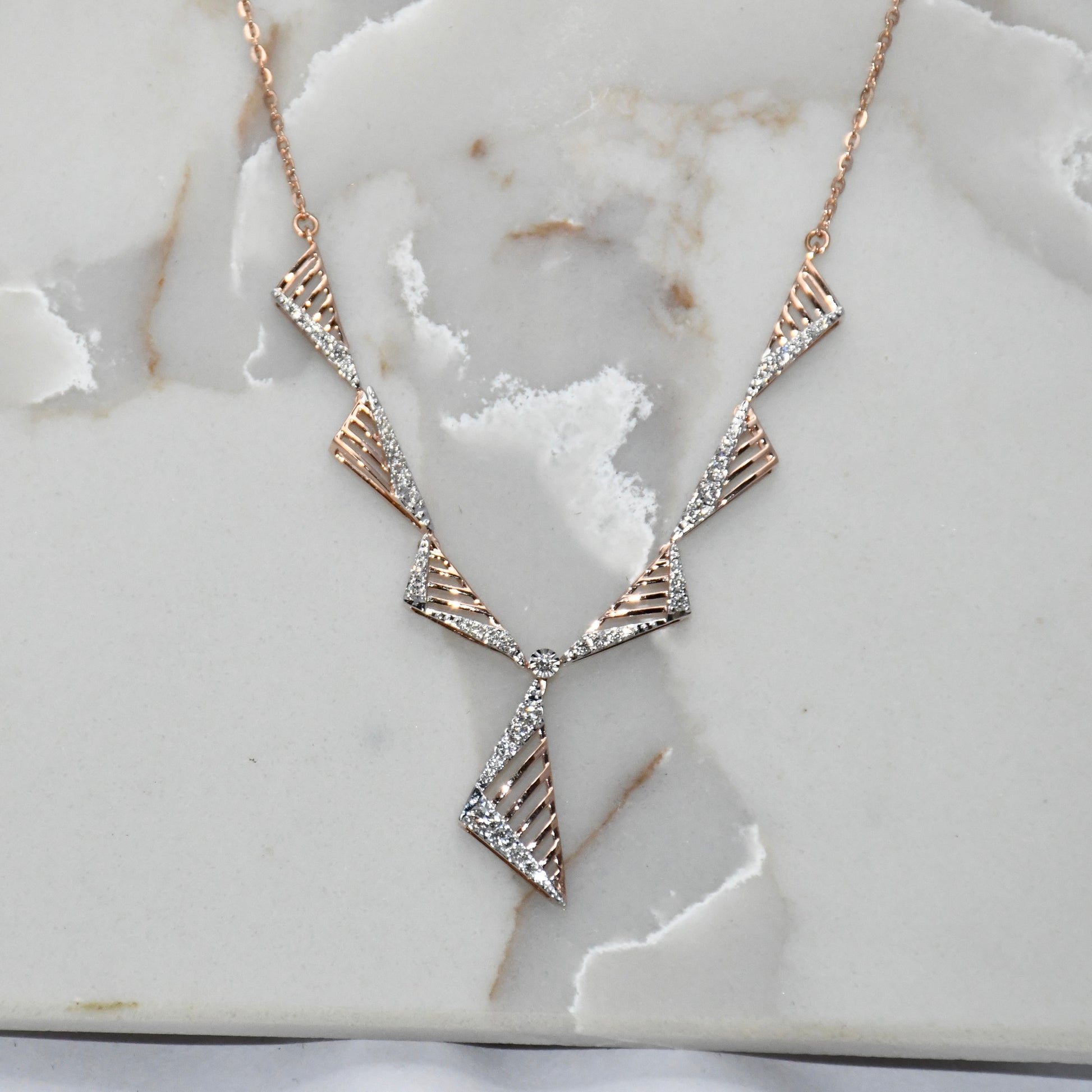 Geometric necklace with rose gold and diamond accents on a marble surface.