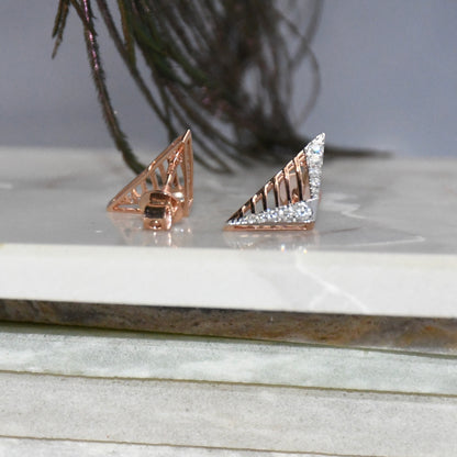 Rose gold diamond earrings on a marble surface with a plant in the background.