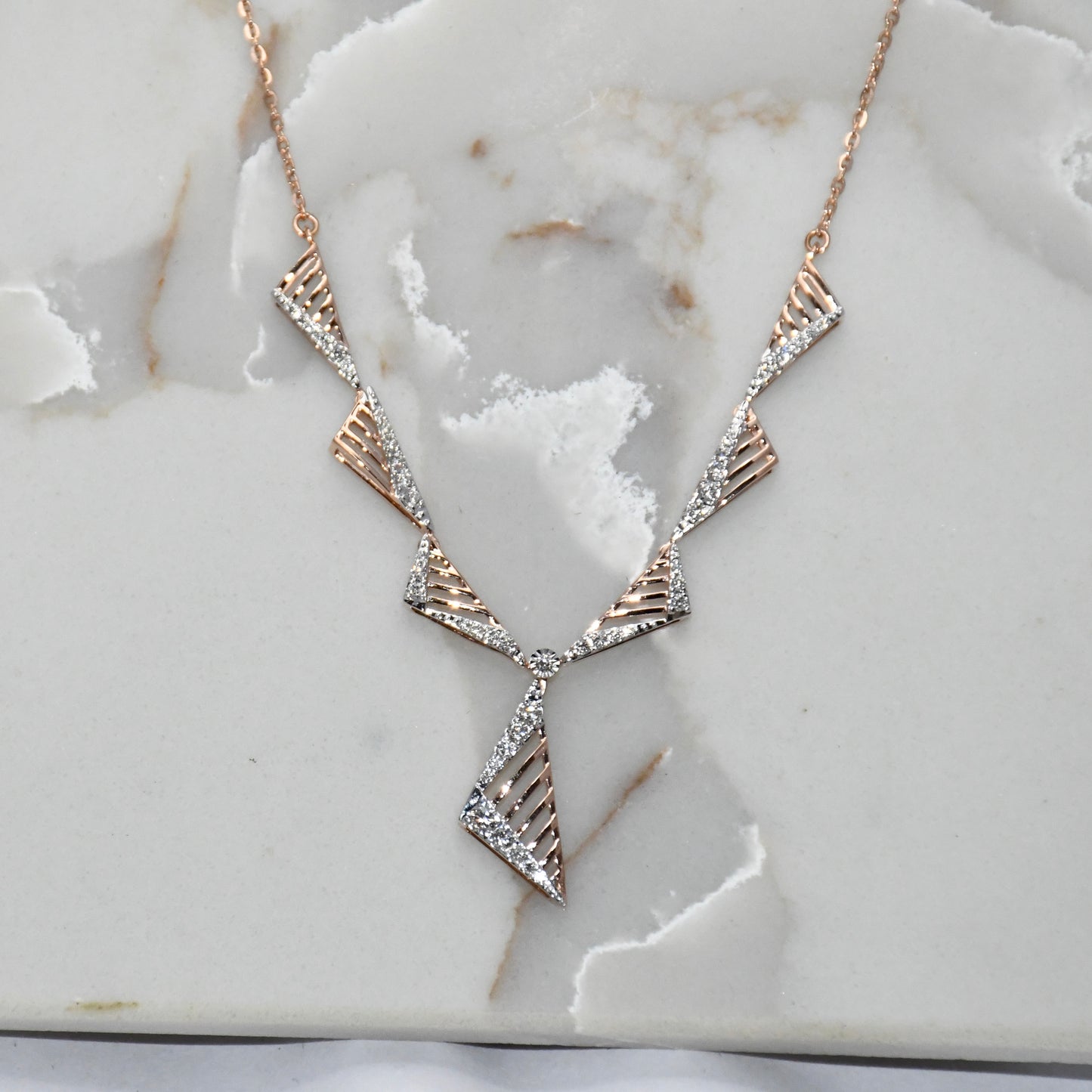 Geometric necklace with gold and diamond accents on a marble surface.