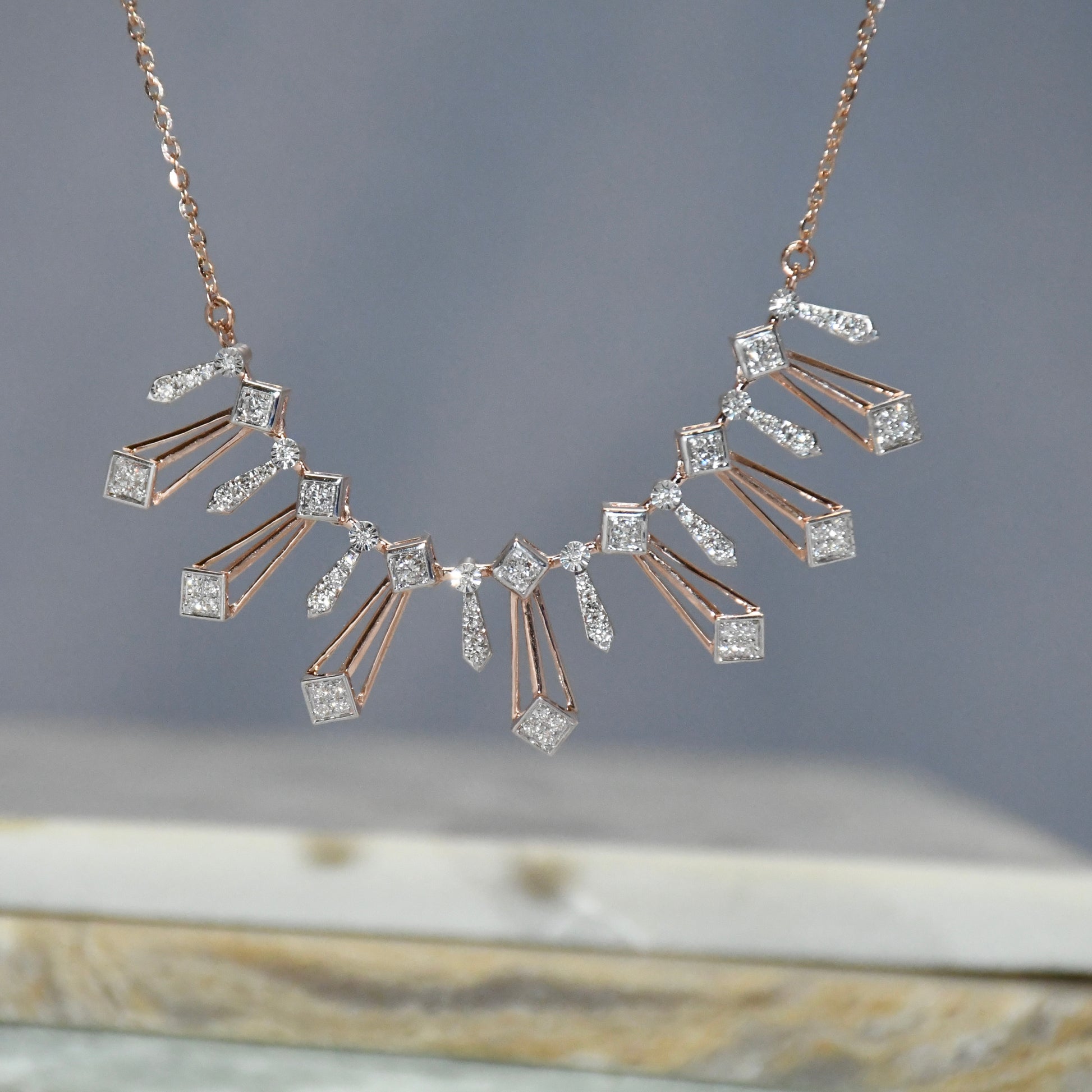 Rose gold necklace with diamonds on a gray background.