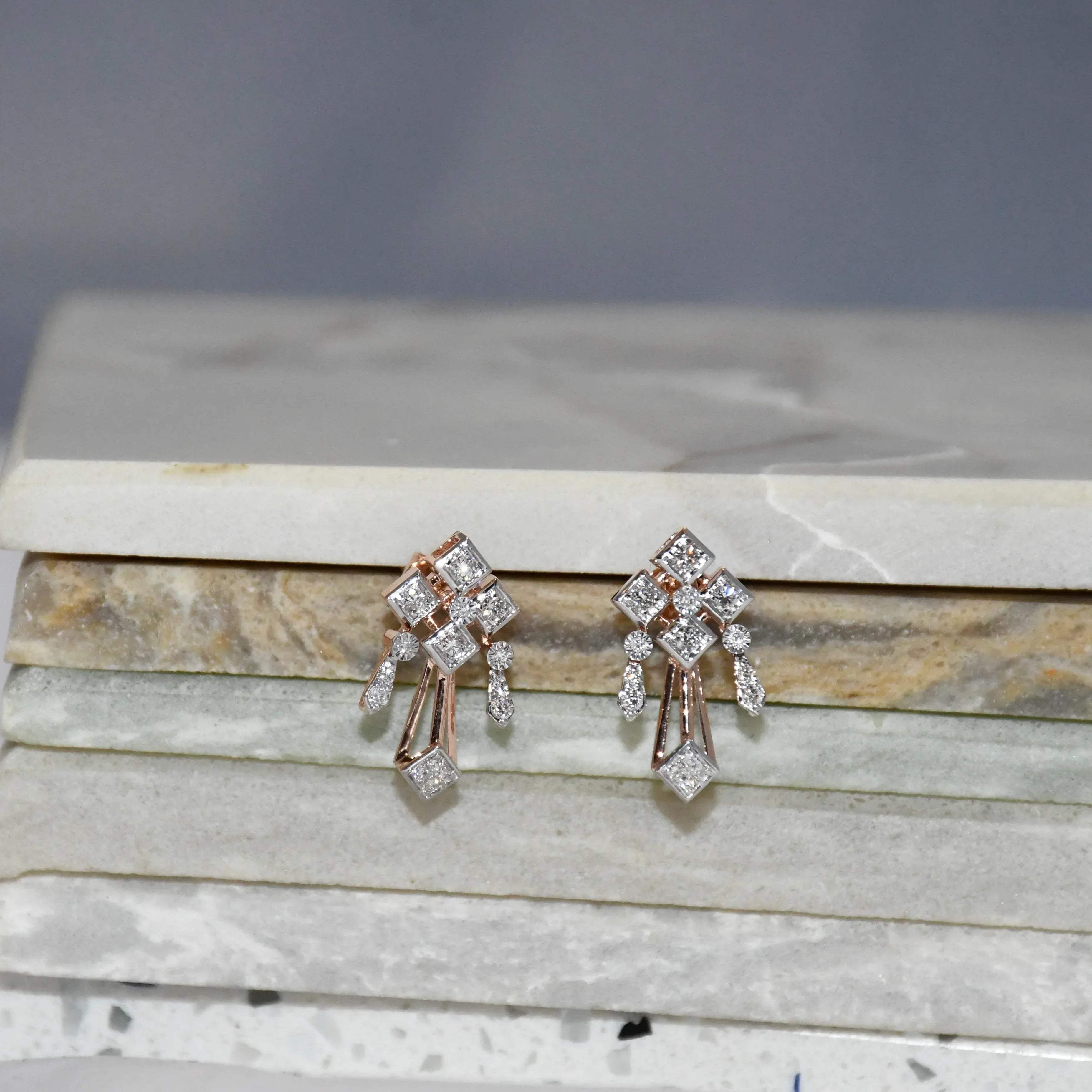 Pair of diamond earrings on a marble surface.