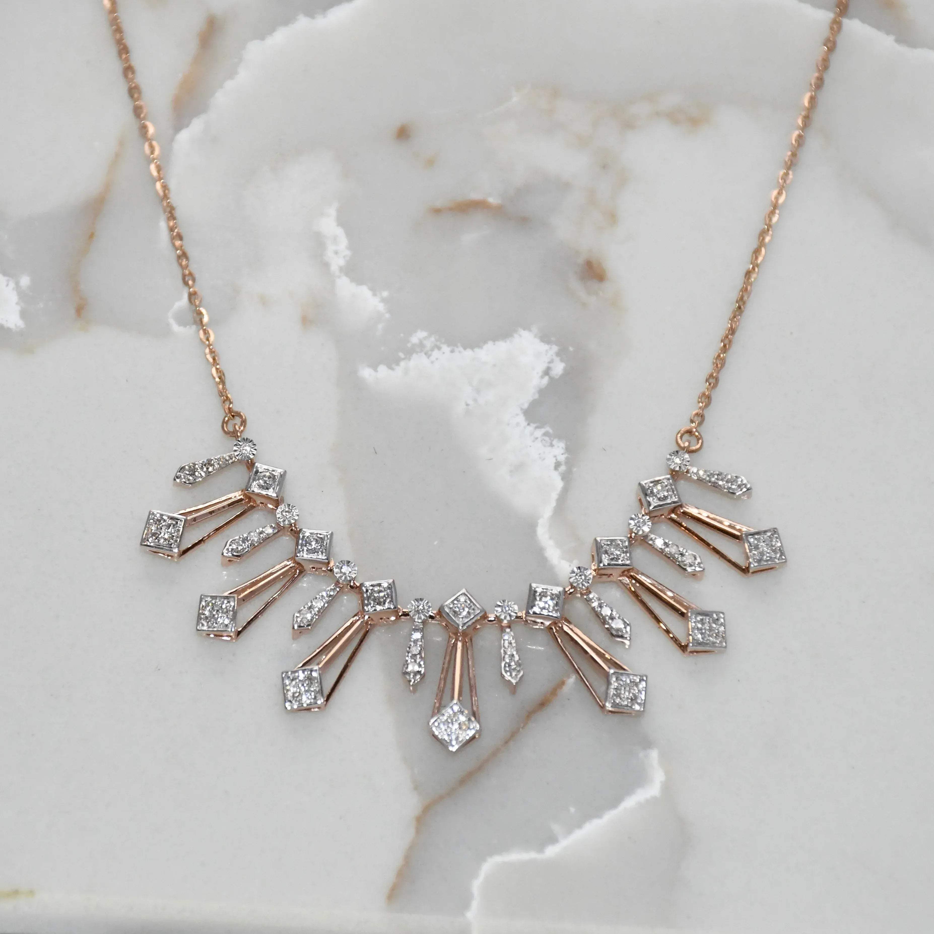 Rose gold necklace with diamond accents on a marble surface