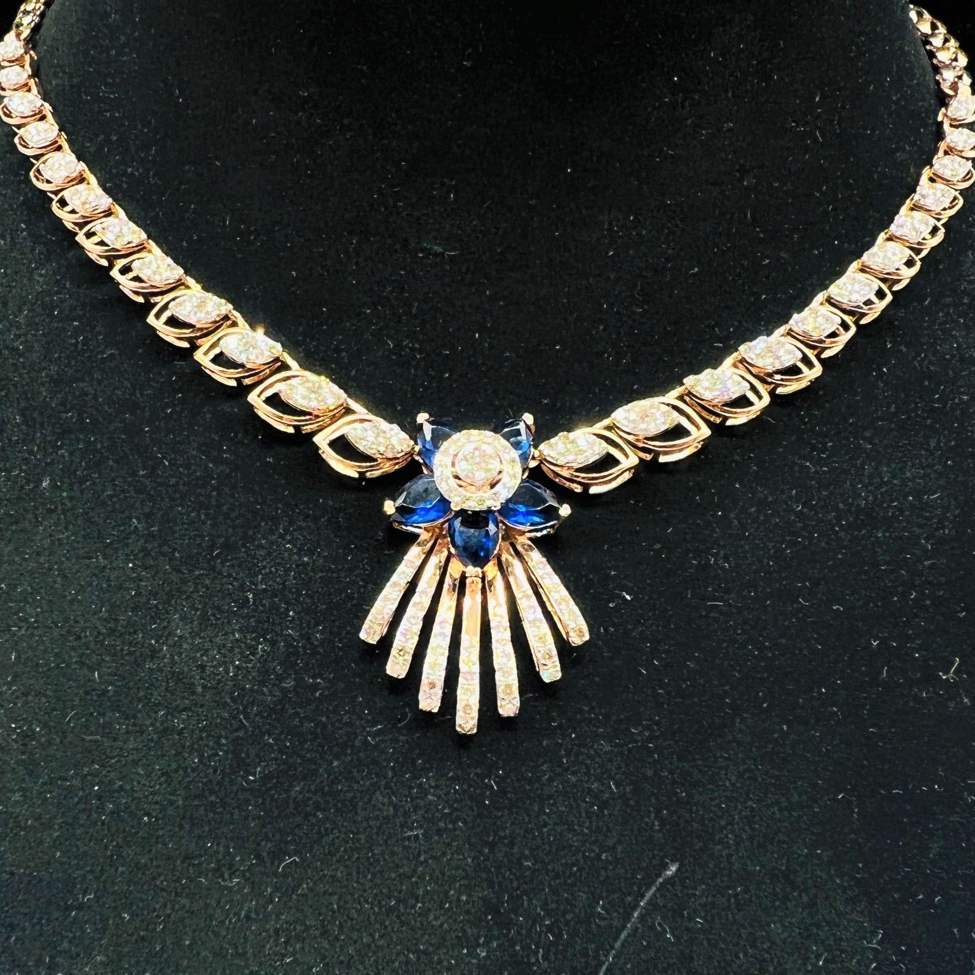 A gold wedding necklace with round-cut blue color stones and clear diamonds displayed on a mannequin bust.