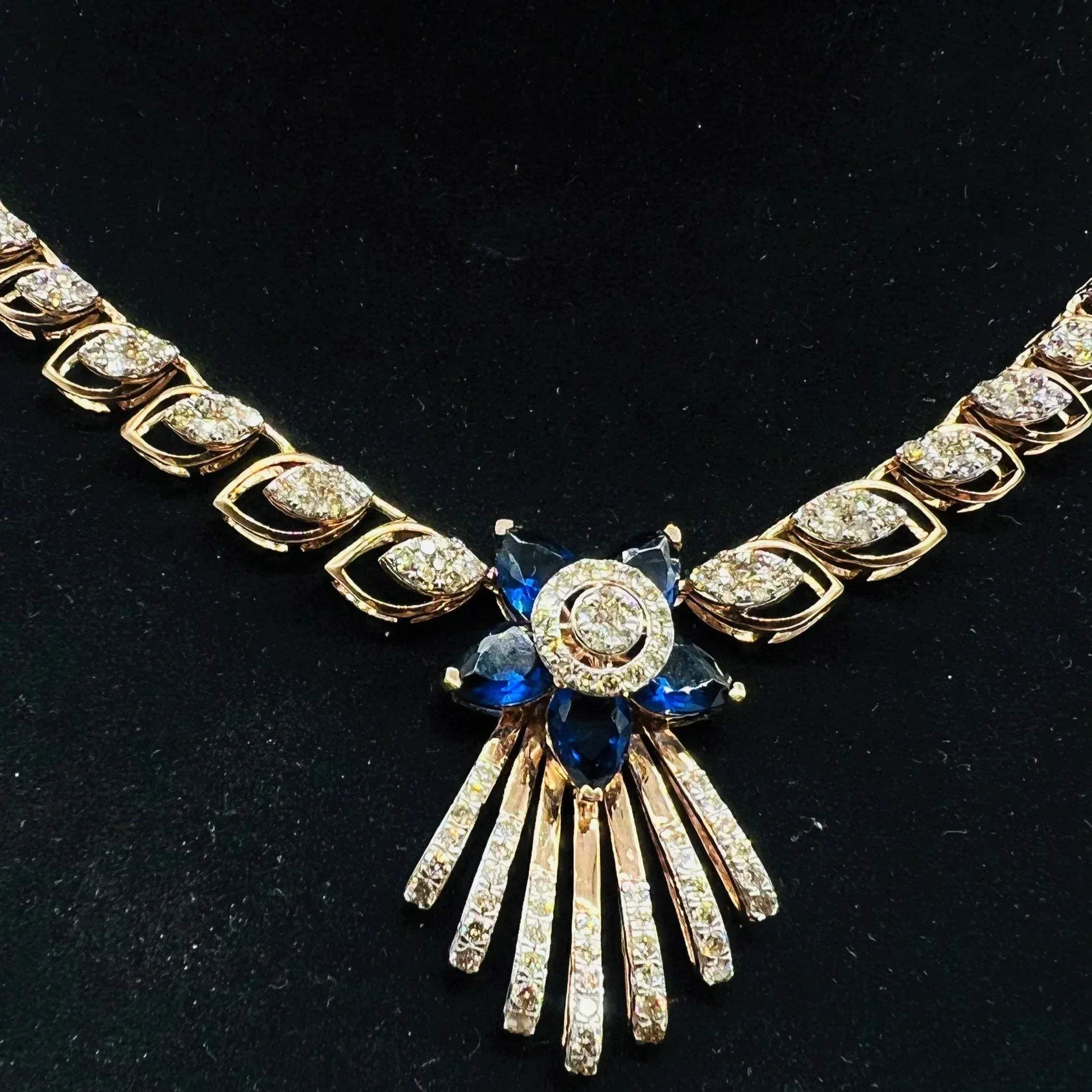 A gold wedding necklace with round-cut blue color stones and clear diamonds displayed on a mannequin bust.