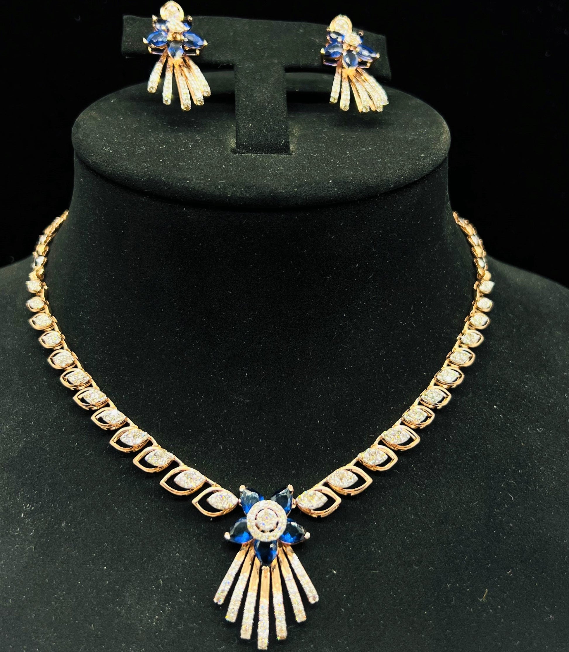 A gold wedding necklace with round-cut blue color stones and clear diamonds with matching earrings displayed on a mannequin bust.
