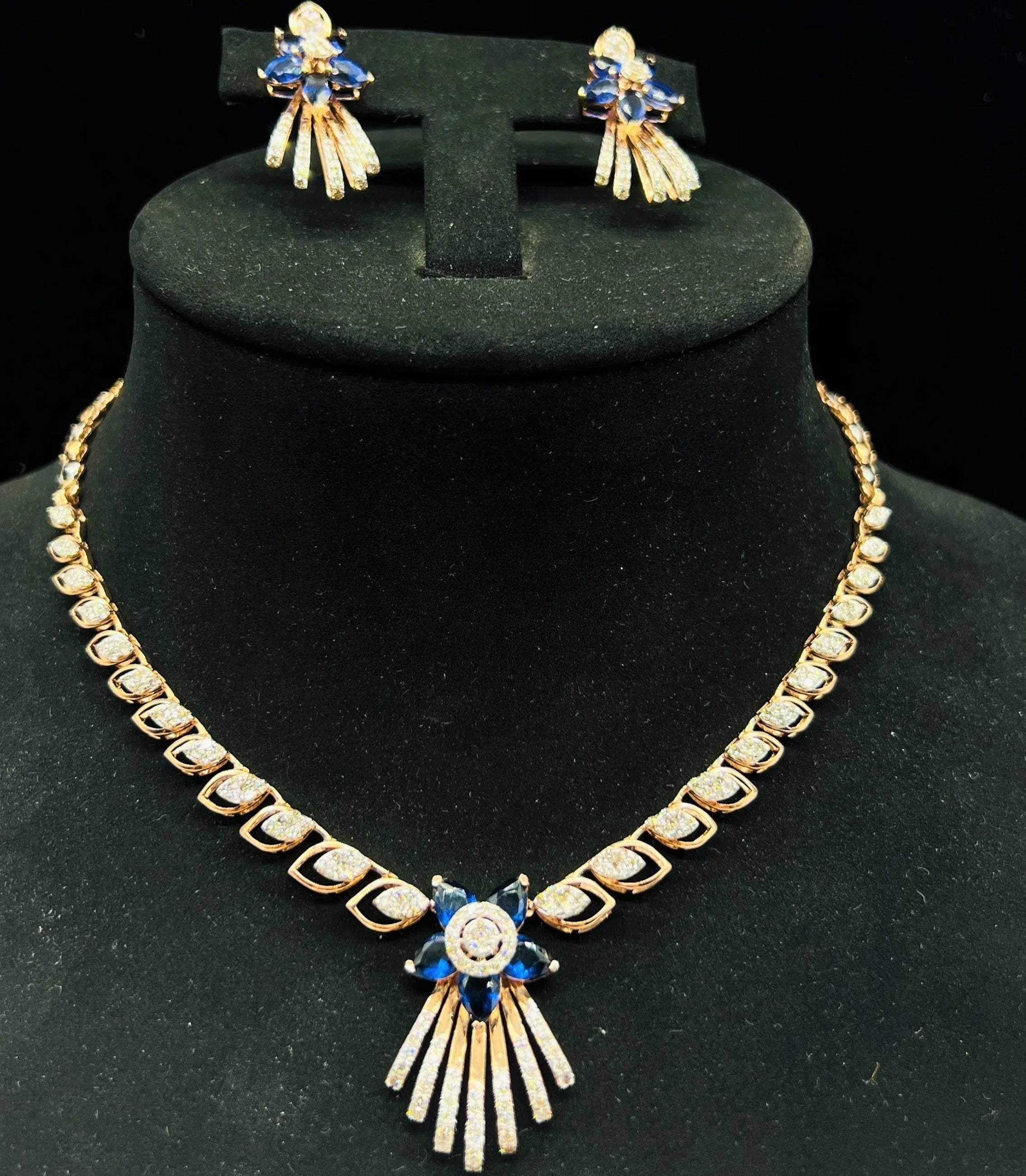 A gold wedding necklace with round-cut blue color stones and clear diamonds with matching earrings displayed on a mannequin bust.