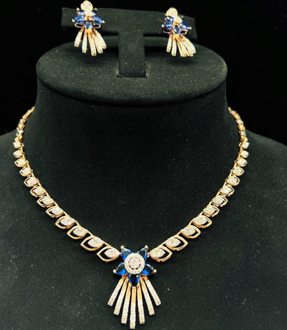 A gold wedding necklace with round-cut blue color stones and clear diamonds with matching earrings displayed on a mannequin bust.