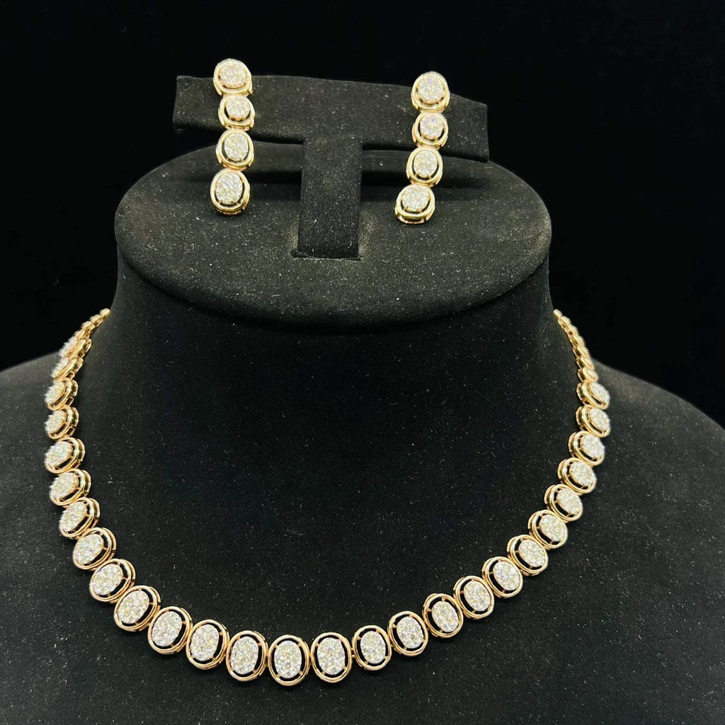 Gold diamond necklace set with matching earrings featuring oval-shaped, pavé-set diamonds in rose gold. The necklace has a linked design showcasing these sparkling stones evenly spaced. Earrings mirror the necklace stones in a vertical stack, creating an elegant accessory set on a black velvet background.