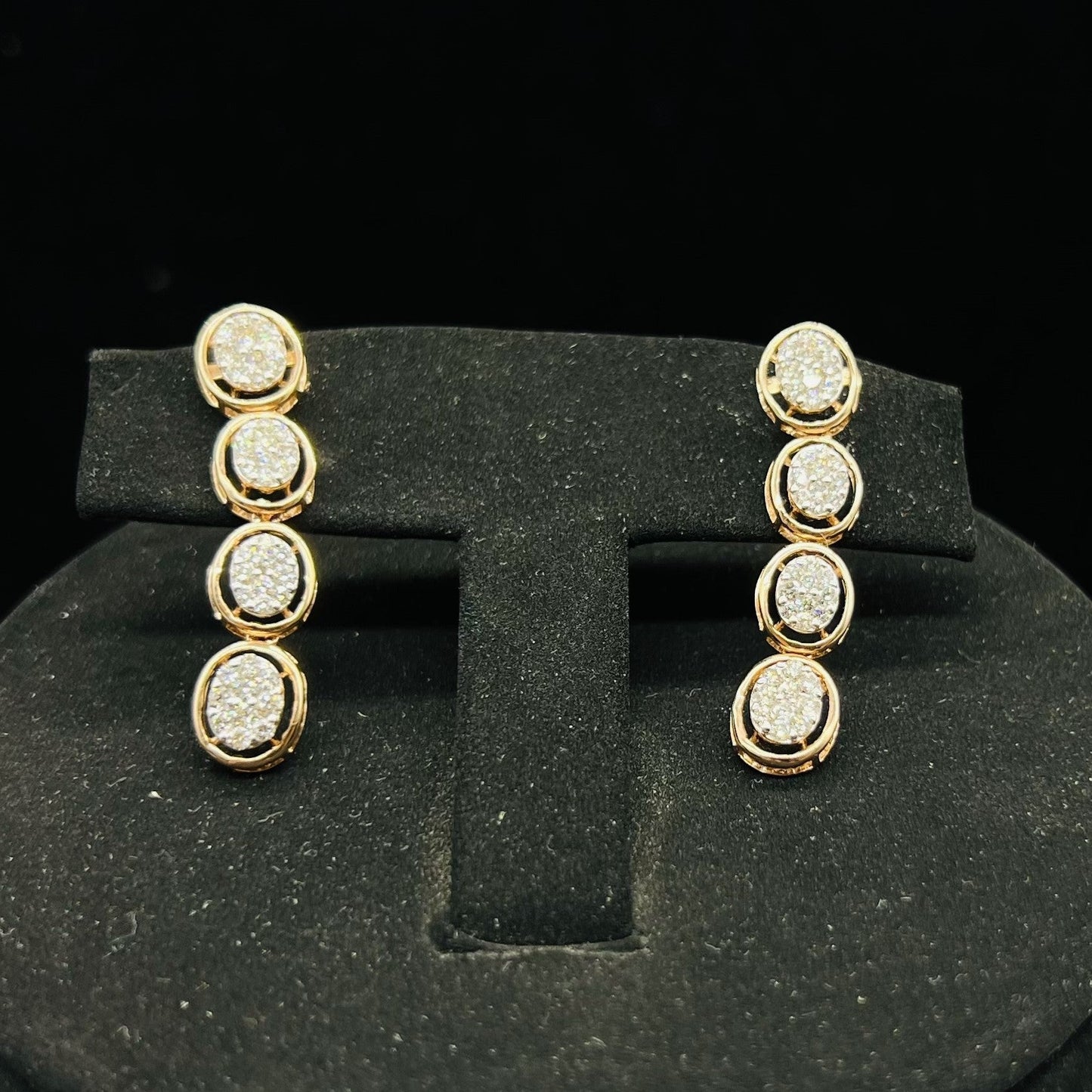 Gold diamond earrings set featuring oval-shaped, pavé-set diamonds in rose gold. The earrings has a linked design showcasing these sparkling stones evenly spaced. Earrings mirror the necklace stones in a vertical stack, creating an elegant accessory set on a black velvet background.